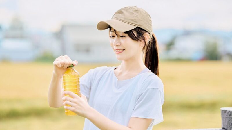 屋外で運動着の女性がペットボトル飲料を開けようとしている写真