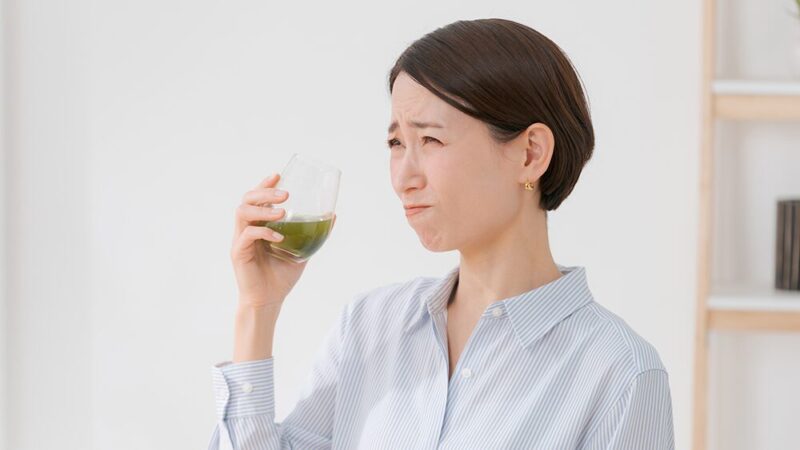 緑の飲み物を飲んで苦そうな表情をしている女性の写真