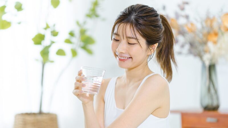 笑顔の女性が水の入ったコップを持っている写真