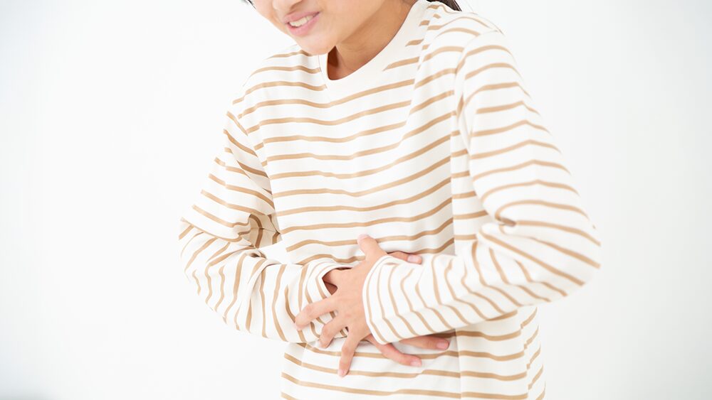 苦悶の表情でおなかにt両手を当てる子どもの写真