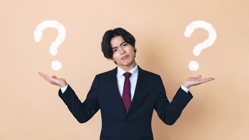 両手に「？マーク」を抱えた、怪訝な表情をした男性の写真