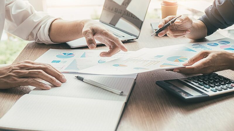 グラフが書いてある資料を見せて話し合っている男性2人の写真