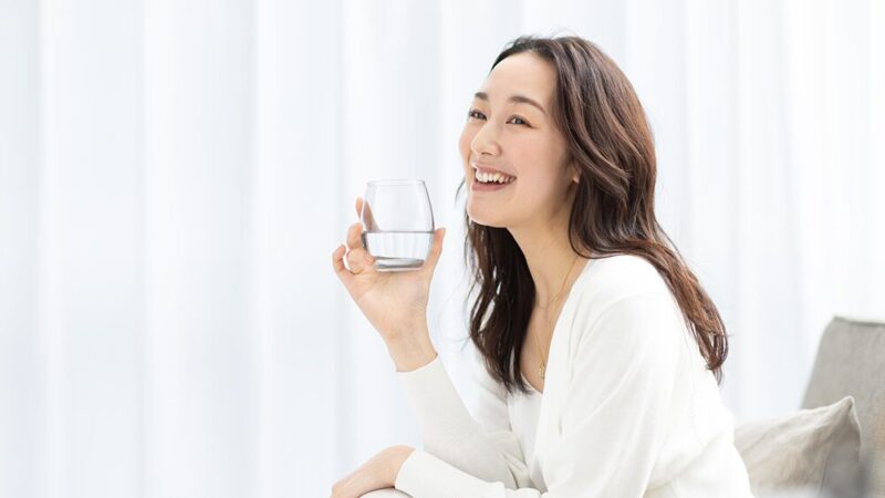 笑顔の女性が右手に水の入ったコップを持っている写真