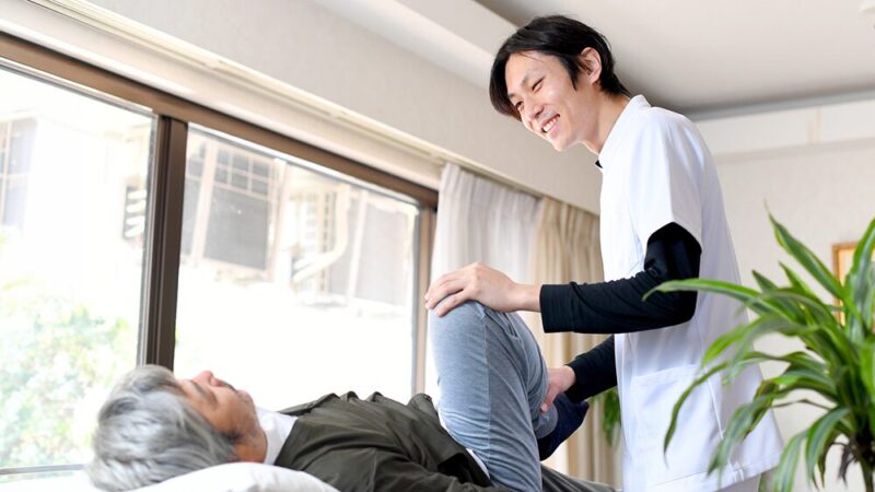 シニア男性の足のストレッチをする整体師の写真